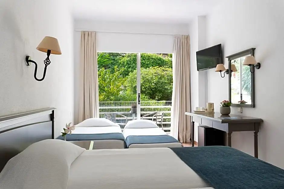 Hotelzimmer mit mehreren Betten, Schreibtisch und Balkonaussicht.
