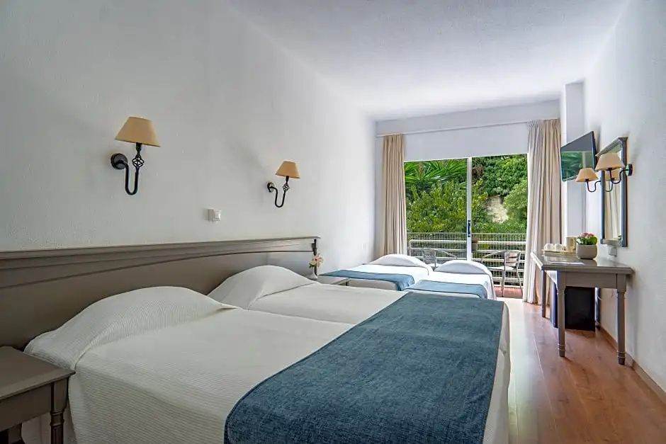 Hell eingerichtetes Hotelzimmer mit mehreren Betten und Zugang zum Balkon.