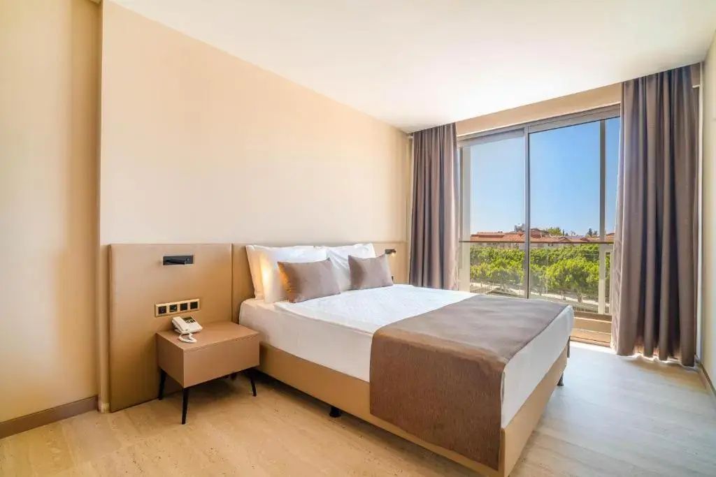 Doppelbett im hell eingerichteten Hotelzimmer mit Nachttisch und Balkontür.