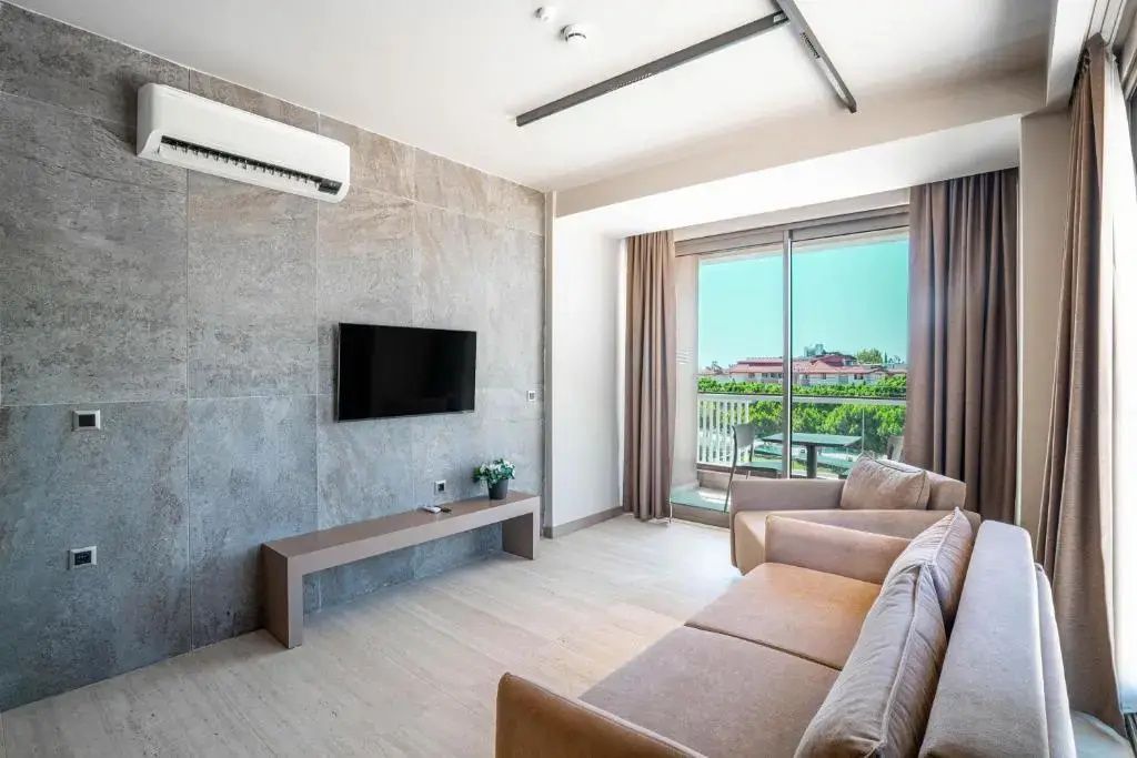 Wohnbereich einer Suite mit Sofa, TV an einer Steinwand und Balkontür.