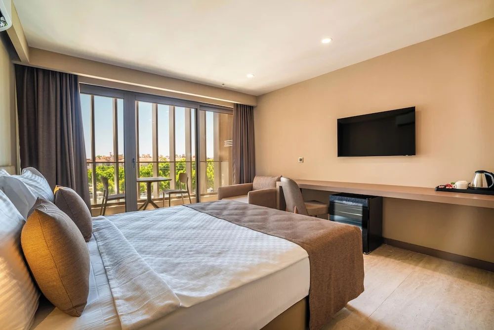 Modernes Hotelzimmer mit Flachbild-TV, Schreibtisch und Balkon mit Sitzgelegenheit.