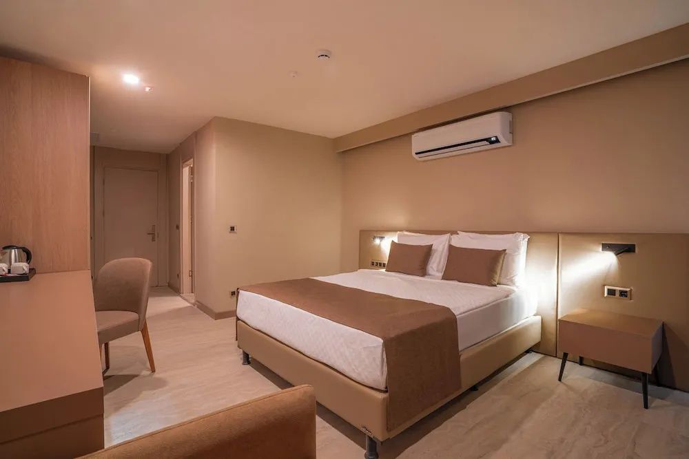 Hell eingerichtetes Hotelzimmer mit Doppelbett, Wandbeleuchtung und Klimaanlage.
