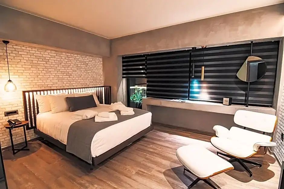 Schlafbereich mit Doppelbett, weißer Backsteinwand und Sessel mit Fußablage.