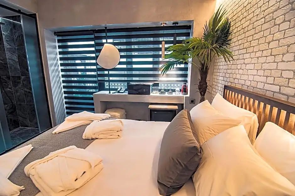 Doppelbett mit weißer Bettwäsche, Kissen und Bademänteln vor einem Fenster mit Jalousie.