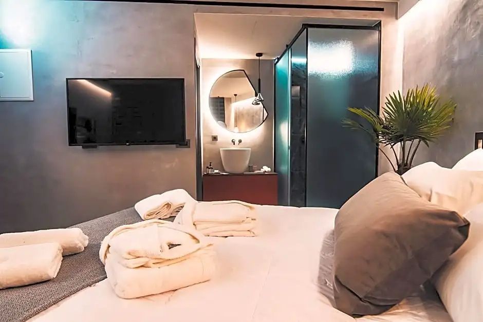 Blick vom Bett auf den offenen Badbereich mit beleuchtetem Rundspiegel an der Betonwand.