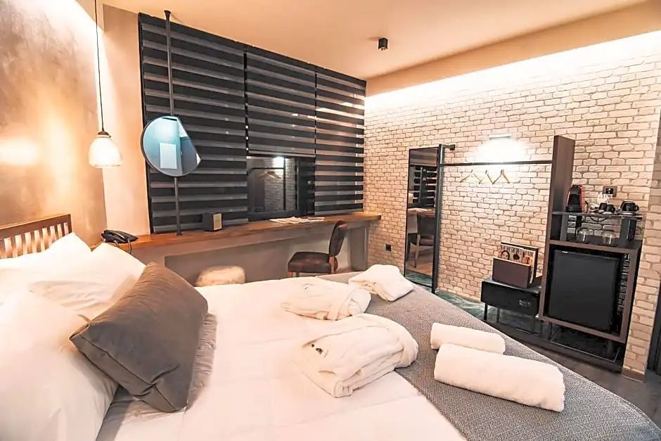 Hotelzimmer mit weiß bezogenem Doppelbett, Schreibtisch am Fenster und Ziegelwand im Hintergrund.