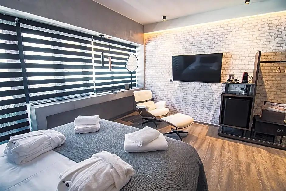 Modern eingerichtetes Hotelzimmer mit Doppelbett, Sessel, Wandfernseher und Backsteinwand.