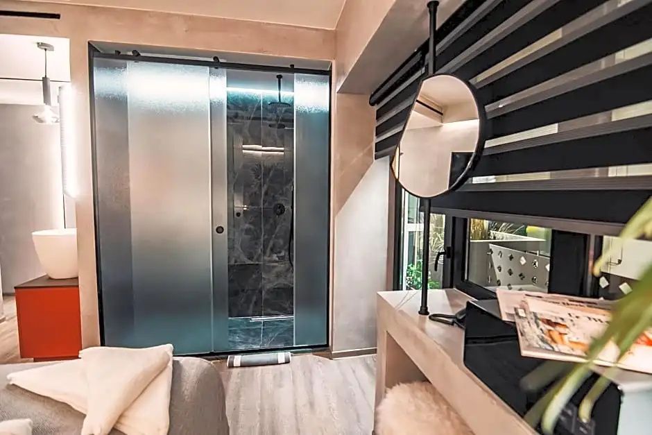 Modernes Hotelzimmer mit Milchglastür zum Badezimmer und einem Kosmetikspiegel am Fenster.
