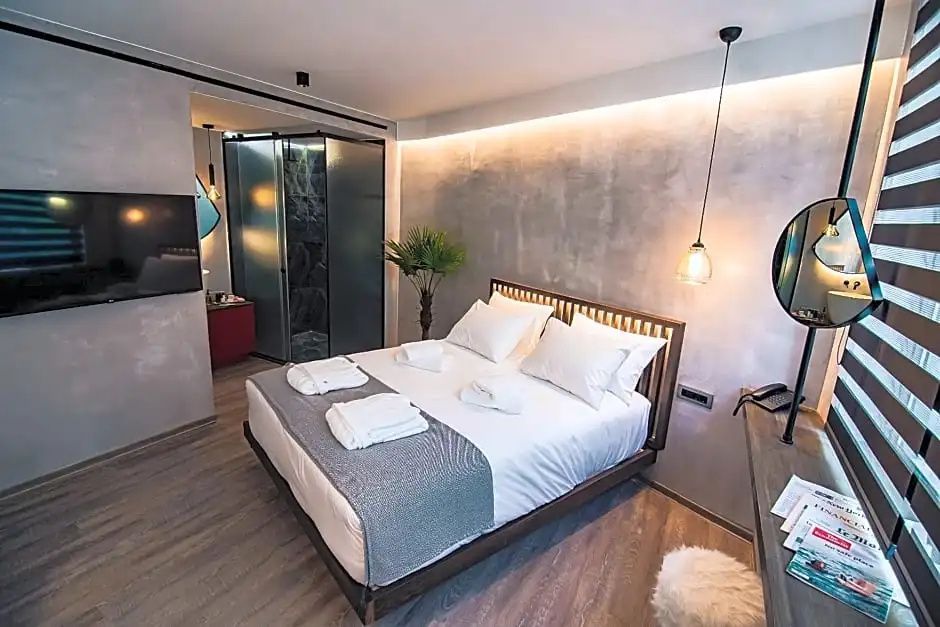 Doppelbett mit Holzkopfteil und weißer Bettwäsche sowie Blick in das angrenzende Badezimmer.