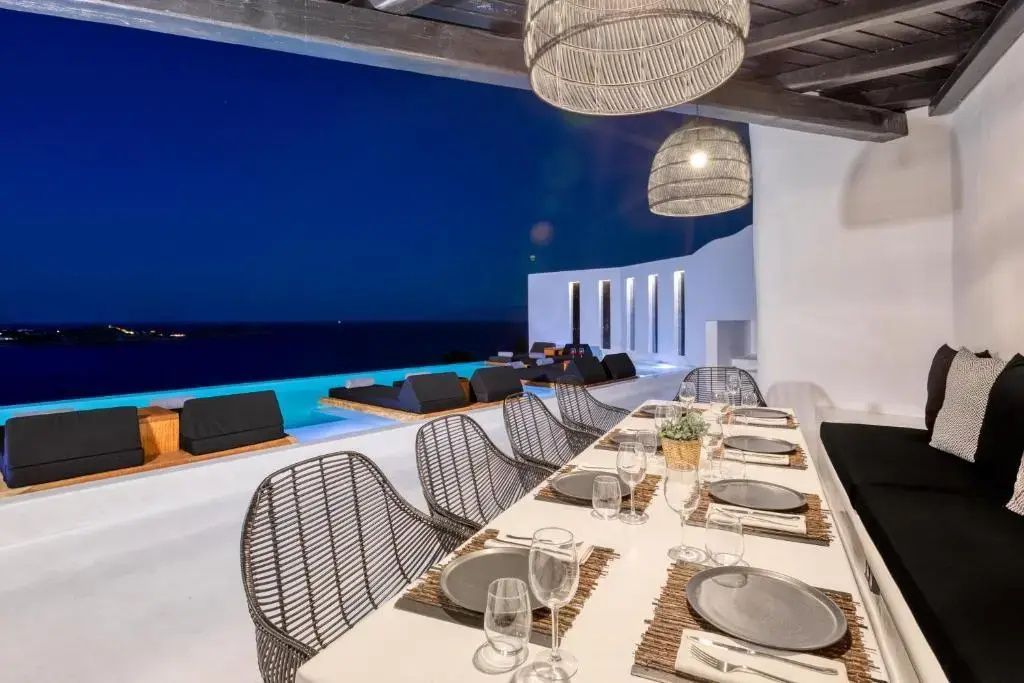 Gedeckter Esstisch auf einer Terrasse am Infinitypool bei Dämmerung mit Blick aufs Meer.