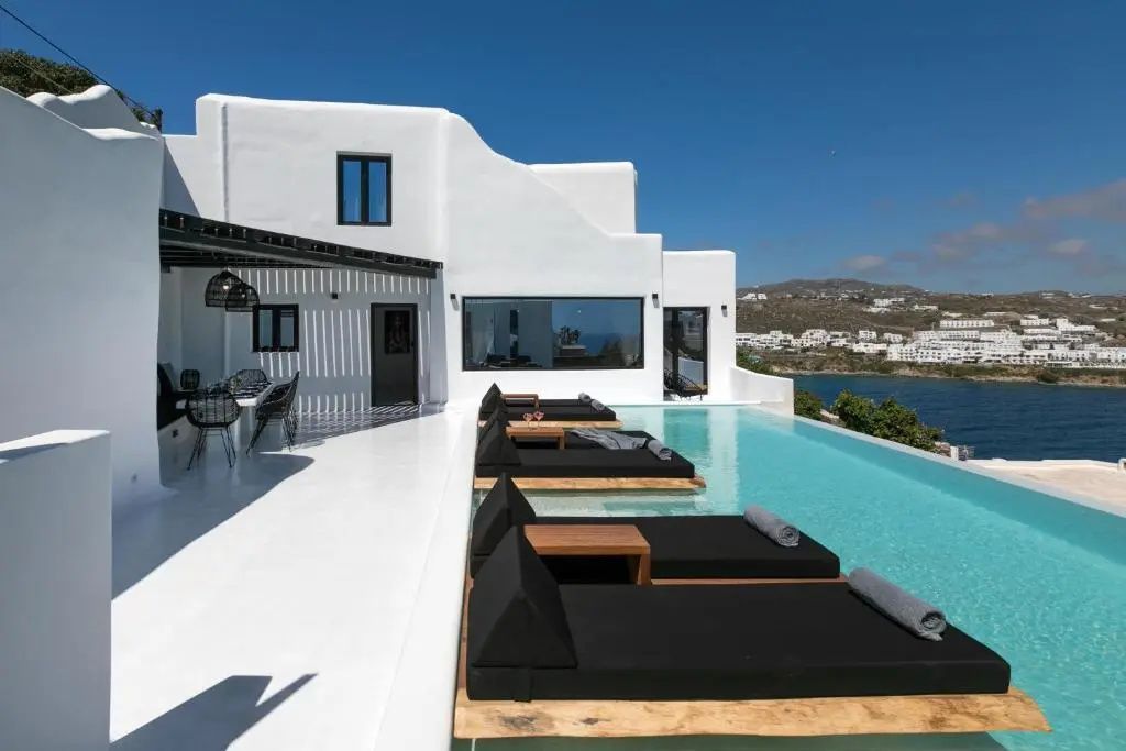 Weiße Villa in kykladischer Architektur mit Pool, schwarzen Liegen und Terrasse.