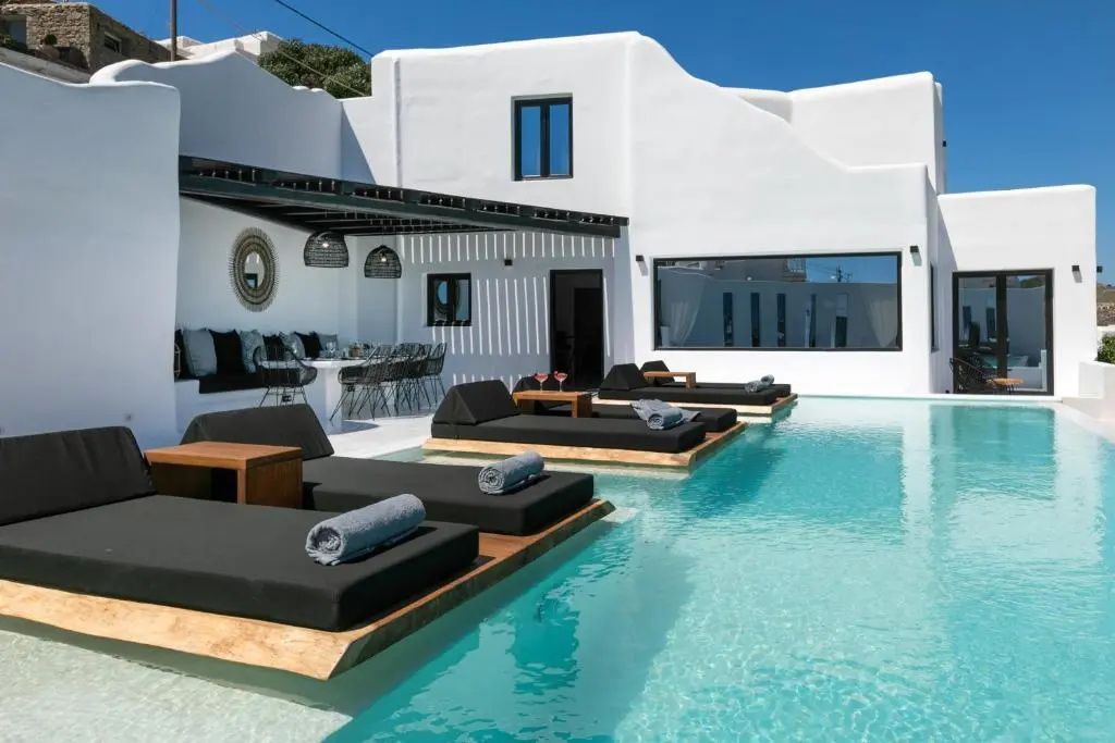 Poolbereich mit schwarzen Sonnenliegen im Wasser vor weißer Terrassenfassade.