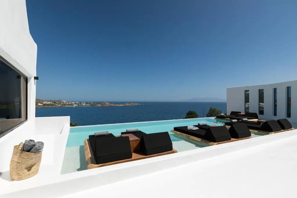 Infinitypool mit dunklen Liegen und freiem Blick auf das blaue Meer unter blauem Himmel.