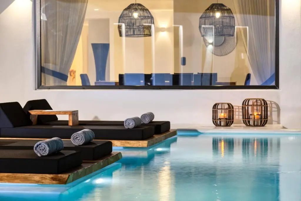 Poolbereich mit ins Wasser ragenden Liegestühlen und Beleuchtung.