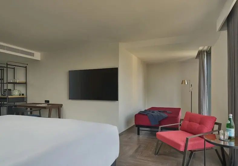 Sitzecke im Hotelzimmer mit rotem Sessel, roter Liege und großem Wandfernseher.