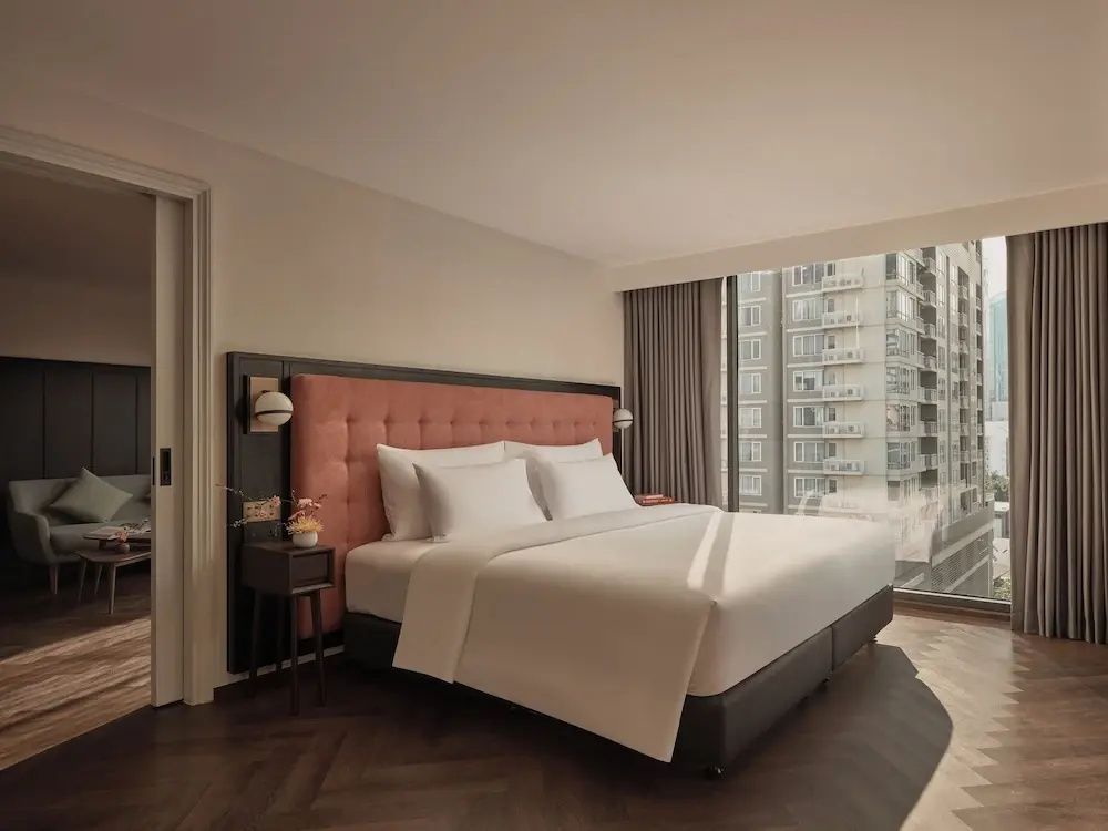 Doppelbett in einem Hotelzimmer mit Holzboden und Blick auf Stadtgebäude.