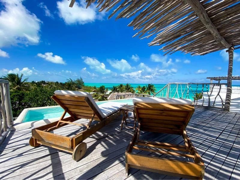 Zwei Holzliegen auf einer schattigen Terrasse mit Blick auf das blaue Meer.