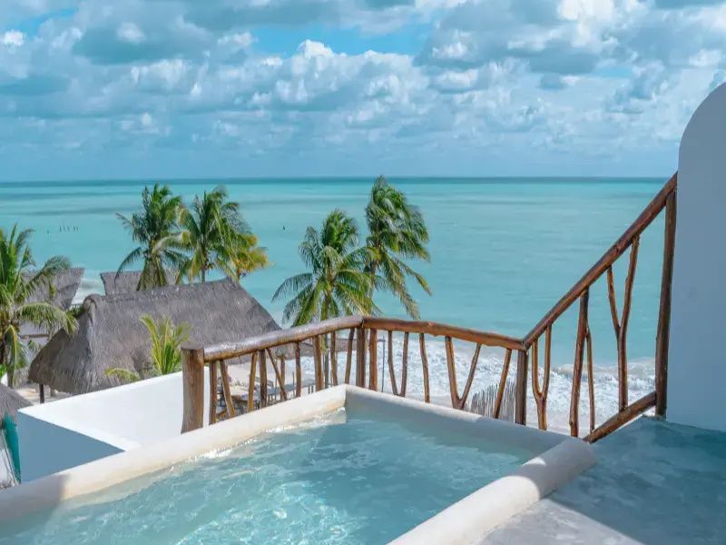Dachterrasse mit einem kleinen Pool, Holzgeländer und Blick auf Palmen sowie das Meer.