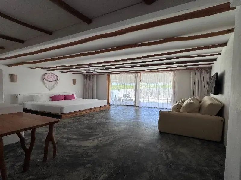 Großzügiges Schlafzimmer mit Doppelbett, rosa Kissen, Sofa und Holzgebälk an der Decke.