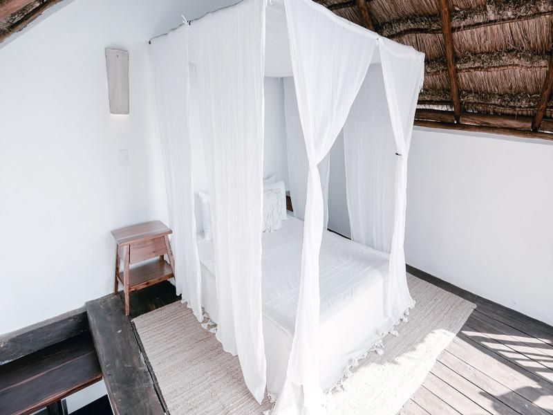 Helles Hotelzimmer mit weiß geschmücktem Himmelbett und Reetdachakzenten.