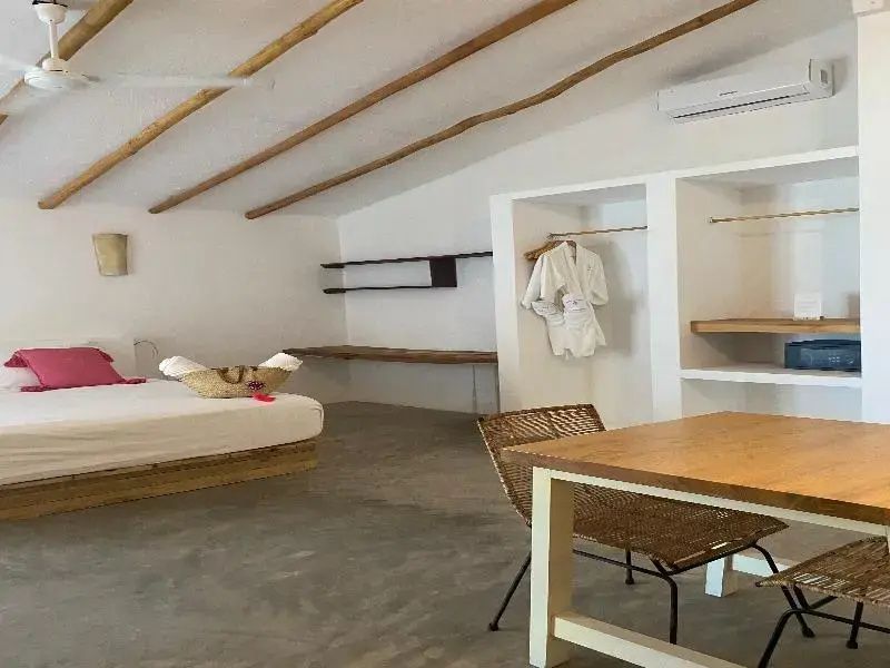 Helles Hotelzimmer mit Holzbalkendecke, weißem Bett und offenem Kleiderschrank.