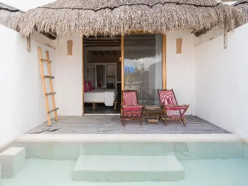 Bungalow mit Reetdach, Terrasse mit zwei Stühlen und direktem Zugang zum Pool.