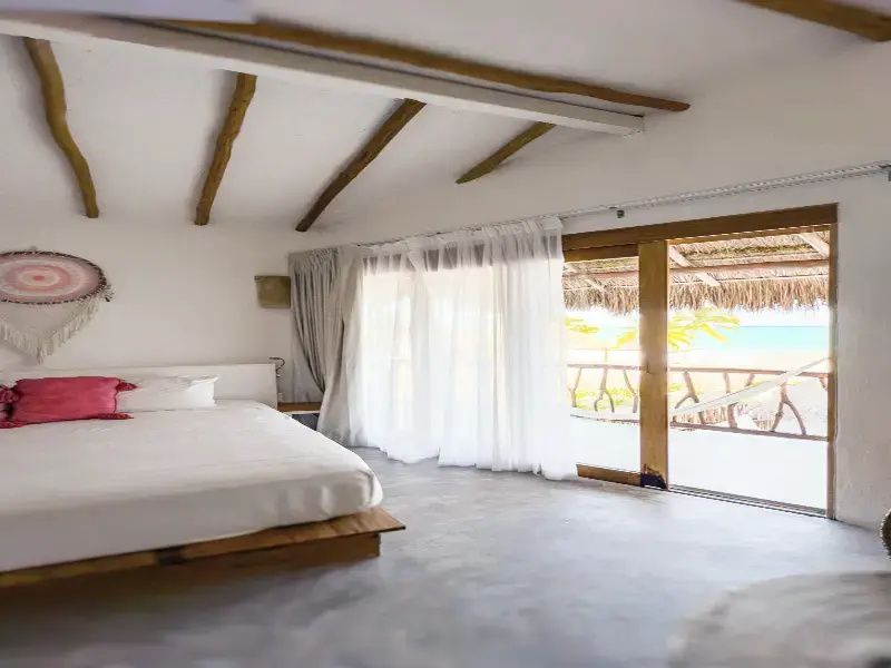 Helles Schlafzimmer mit Doppelbett, Holzbalken und Blick auf die Terrasse zum Meer.