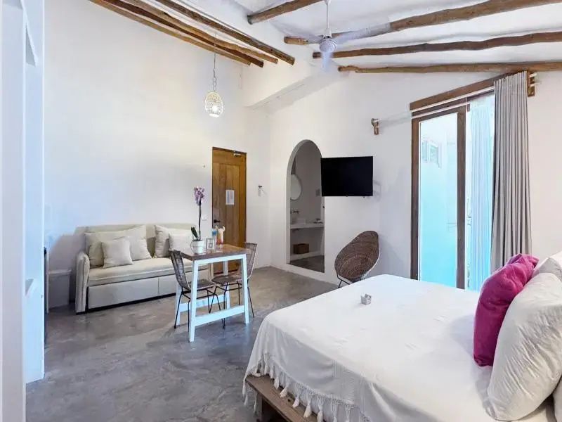 Geräumiges Zimmer mit Holzbalkendecke, kleinem Esstisch, Sofa und großem Bett.