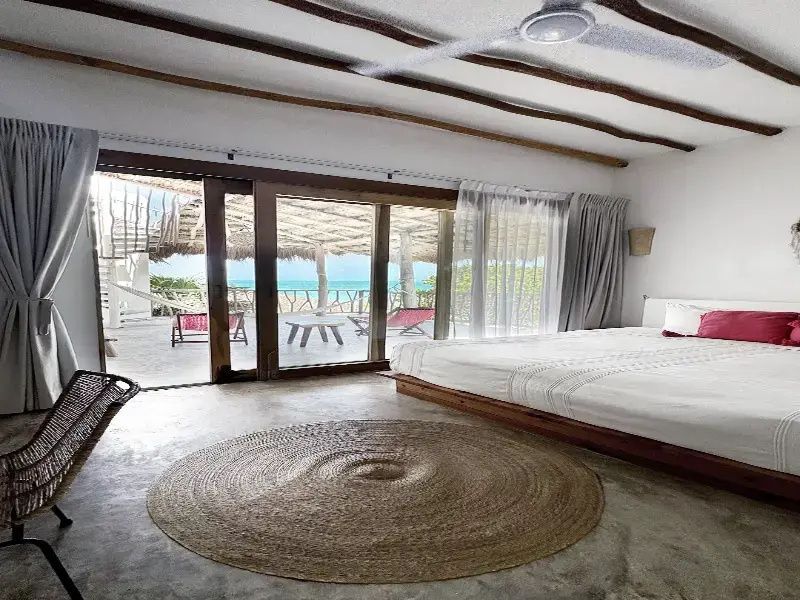 Geräumiges Schlafzimmer mit großem Bett, rundem Teppich und Zugang zur Terrasse.