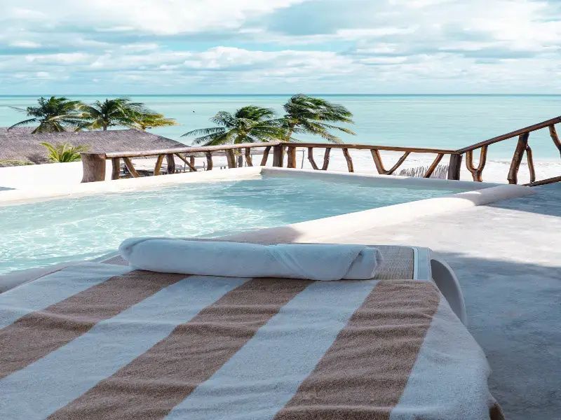 Eine Sonnenliege mit gestreiftem Handtuch an einem Pool mit Aussicht auf das Meer.