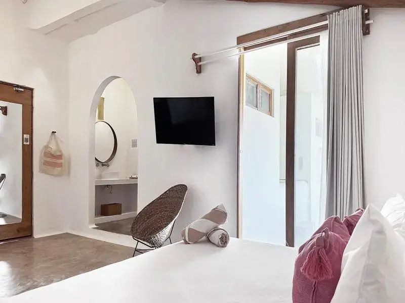 Blick vom Bett mit rosa Kissen auf die Wand mit Fernseher und einen Rundbogen.