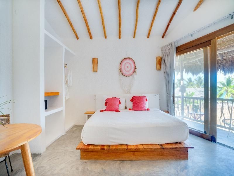 Hell eingerichtetes Schlafzimmer mit Holzdecke, rotem Dekokissen und Traumfänger.
