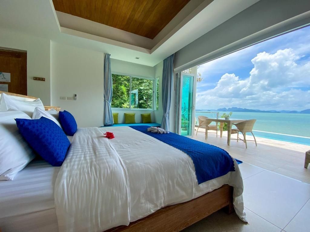Helles Hotelzimmer mit Doppelbett, blauen Akzenten und Blick auf Terrasse und Meer.