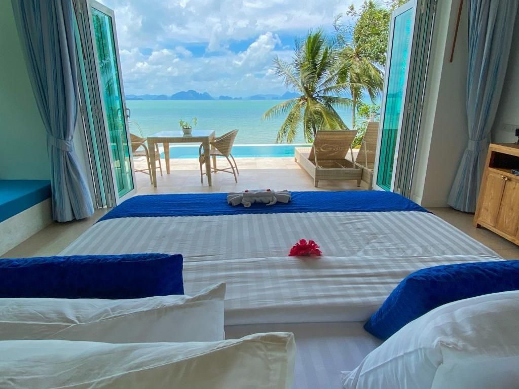 Blick vom Bett durch geöffnete Flügeltüren auf die Terrasse, den Pool und das Meer mit Inseln.