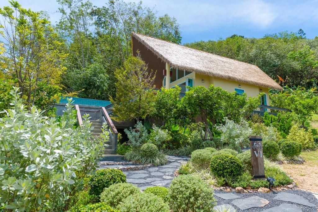 Villa mit Reetdach umgeben von tropischen Pflanzen und einem Steinpfad