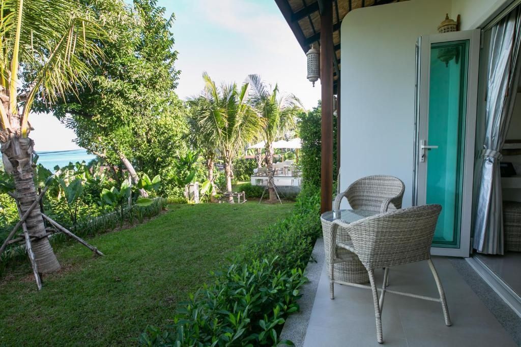 Überdachte Terrasse mit zwei Rattan-Sesseln und Blick auf Rasen und Palmen.