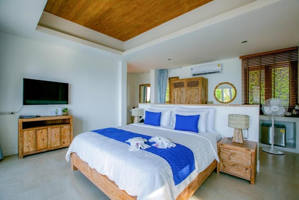 Hotelzimmer mit Holzmöbeln, großem Doppelbett, blauer Tagesdecke und Fernseher.