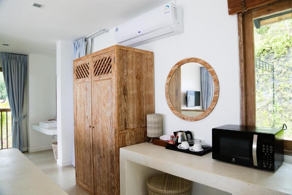 Holzschrank, runder Wandspiegel und Ablage mit Teezubereiter und Mikrowelle im Zimmer.