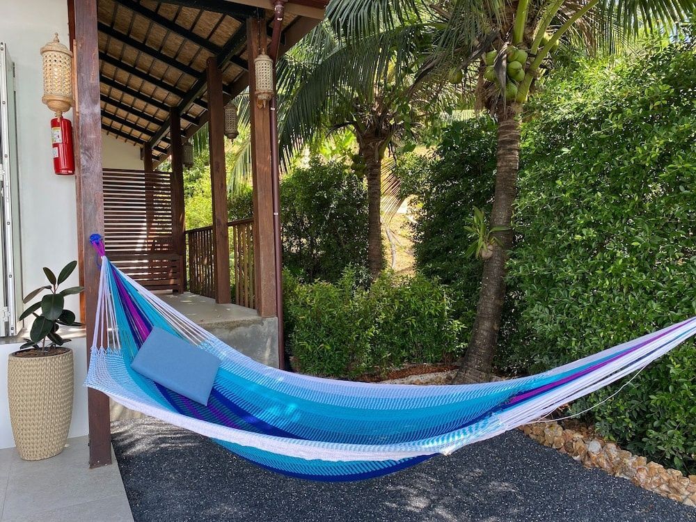 Bunte Hängematte auf einer überdachten Terrasse vor tropischen Pflanzen.