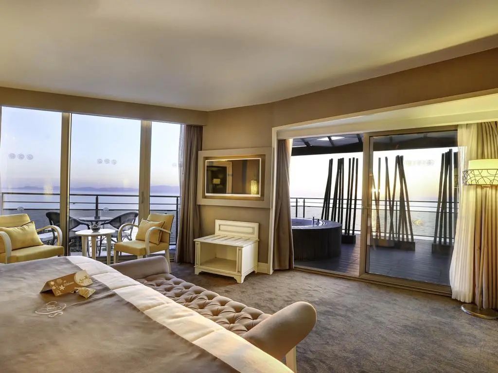 Hotelzimmer mit Doppelbett, Sitzbereich und großen Glasfronten zum Balkon mit Whirlpool.