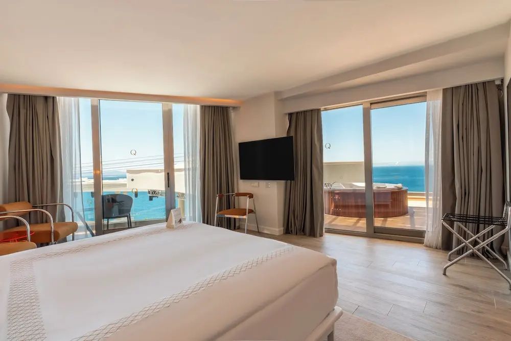 Helles Schlafzimmer mit großem Doppelbett, Fernseher und Balkon zum Meer.