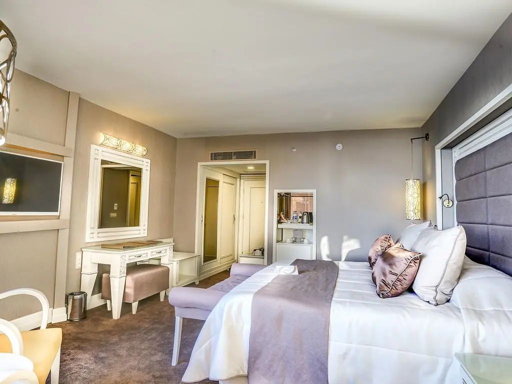 Hotelzimmer mit Doppelbett, Schminktisch und Spiegel unter hellem Licht.
