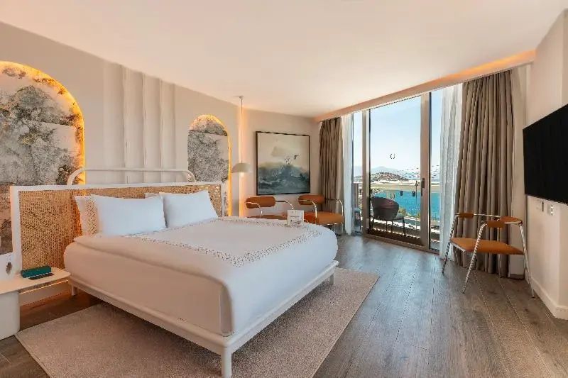 Helles Hotelzimmer mit großem Bett und Verglasung zum Balkon mit Blick auf das Meer.