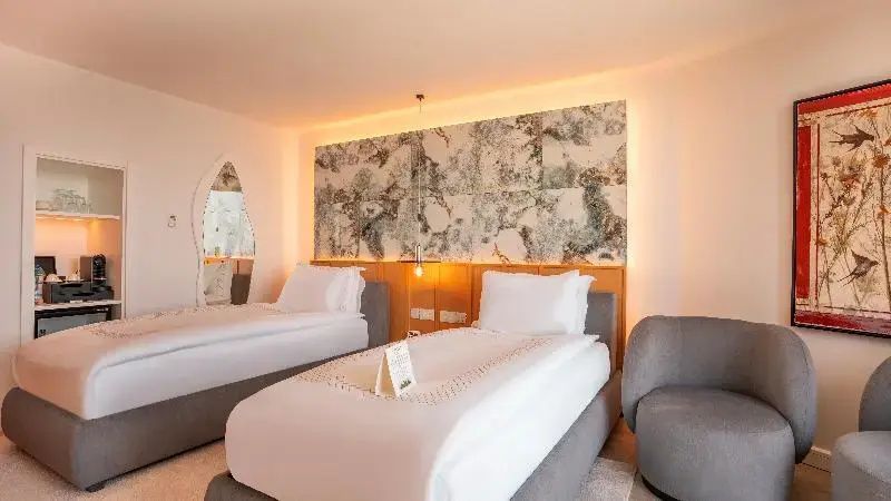 Zwei Einzelbetten in einem hellen Zimmer mit beleuchteter Wanddekoration in Steinoptik.