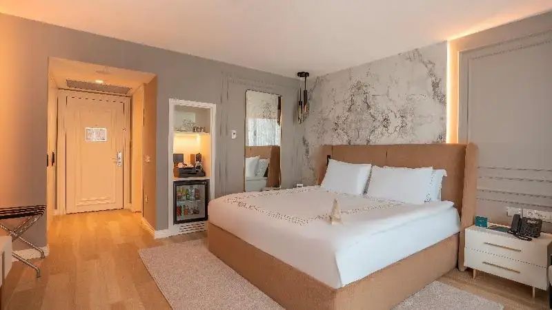 Doppelzimmer mit weißer Bettwäsche, Marmoroptik an der Wand und eingebauter Minibar.
