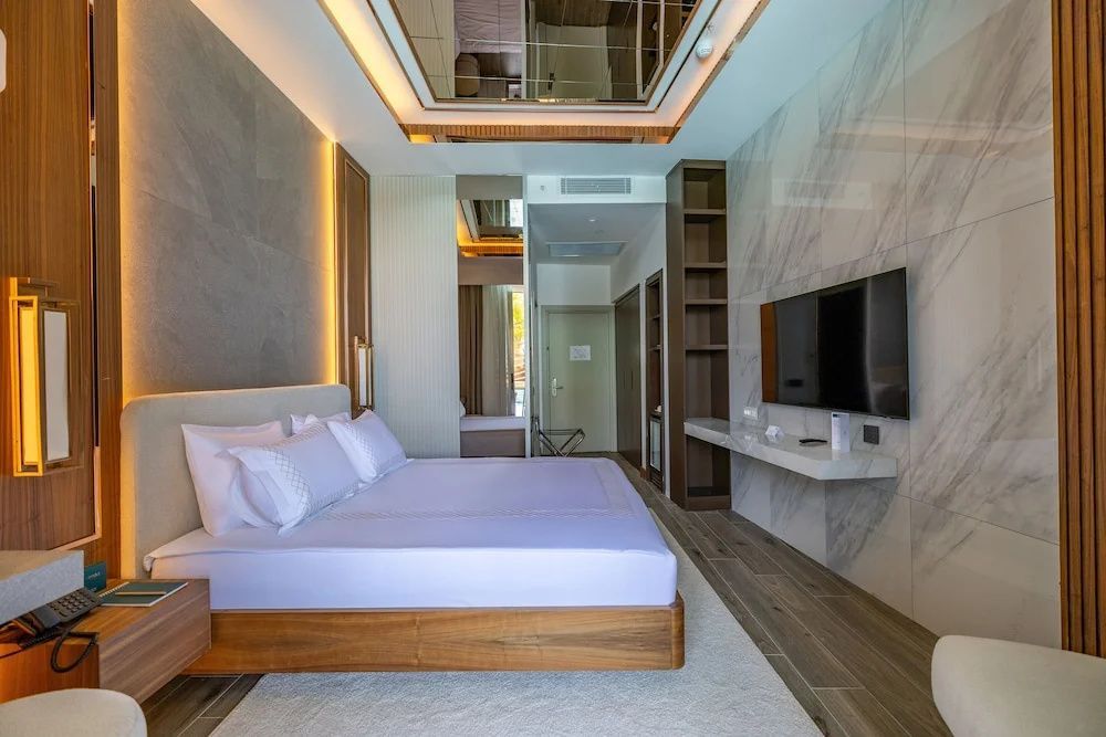 Hotelzimmer mit großem Bett, Fernseher an einer Wand in Marmoroptik und Holzverkleidung.