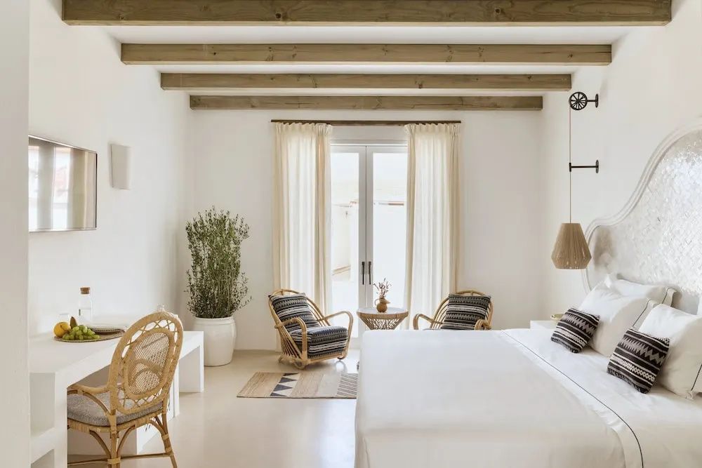 Schlafzimmer mit Doppelbett, Holzdeckenbalken, zwei Korbsesseln und Balkontür.