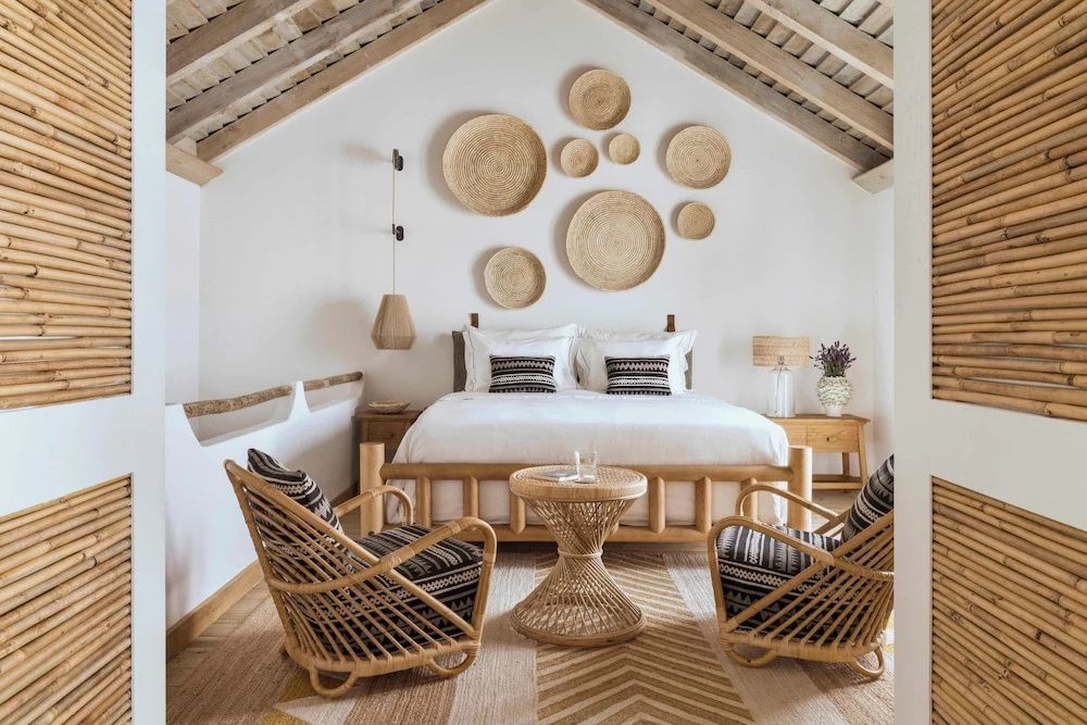 Doppelbett unter einer Dachschräge mit Holzgebälk, dekoriert mit gewebten Wandtellern aus Stroh.