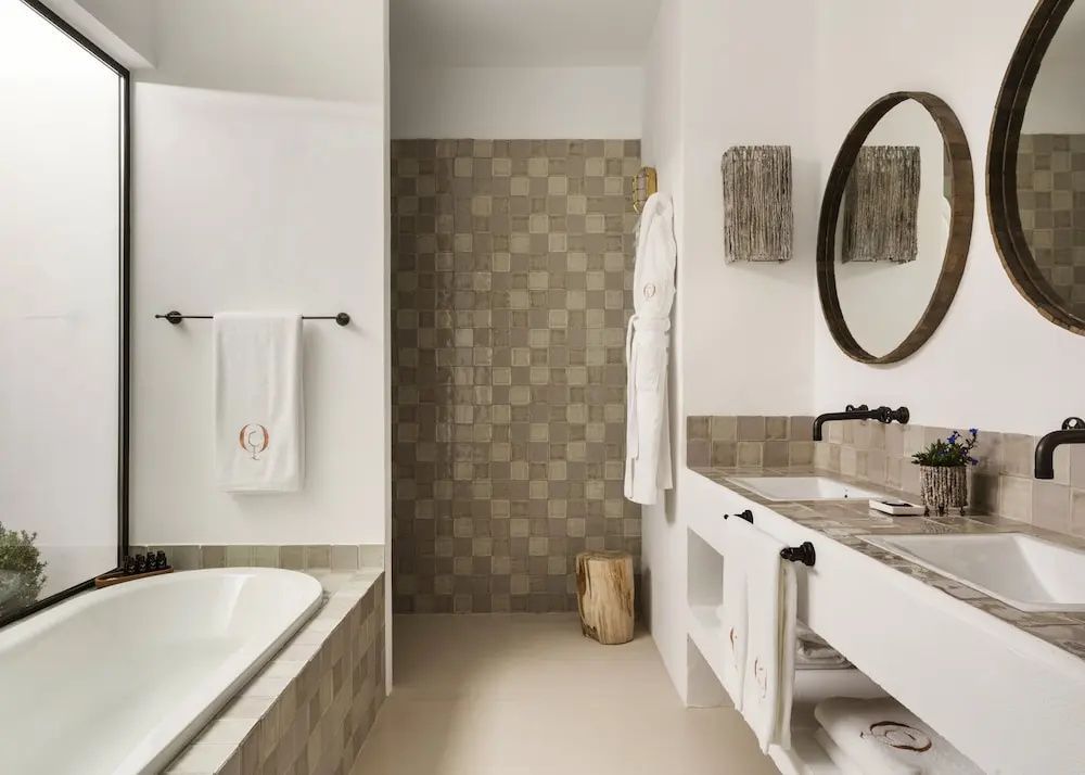 Badezimmer mit hellen Fliesen, Badewanne, Dusche und rundem Spiegel.