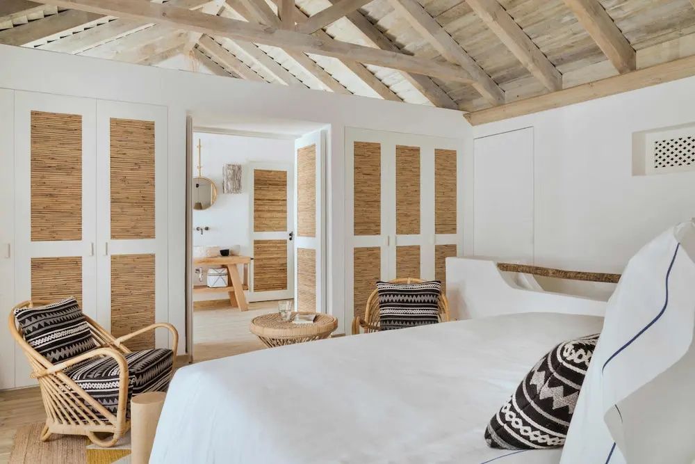 Hell eingerichtetes Schlafzimmer mit Holzdecke, weißem Bett und Blick ins Badezimmer.